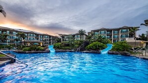A swimming pool with two slides, surrounded by buildings with balconies and tropical landscaping.