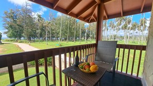 Un balcon avec une table et des chaises, un saladier rempli de fruits, et une vue sur un espace verdoyant avec des arbres et un ciel dégagé.