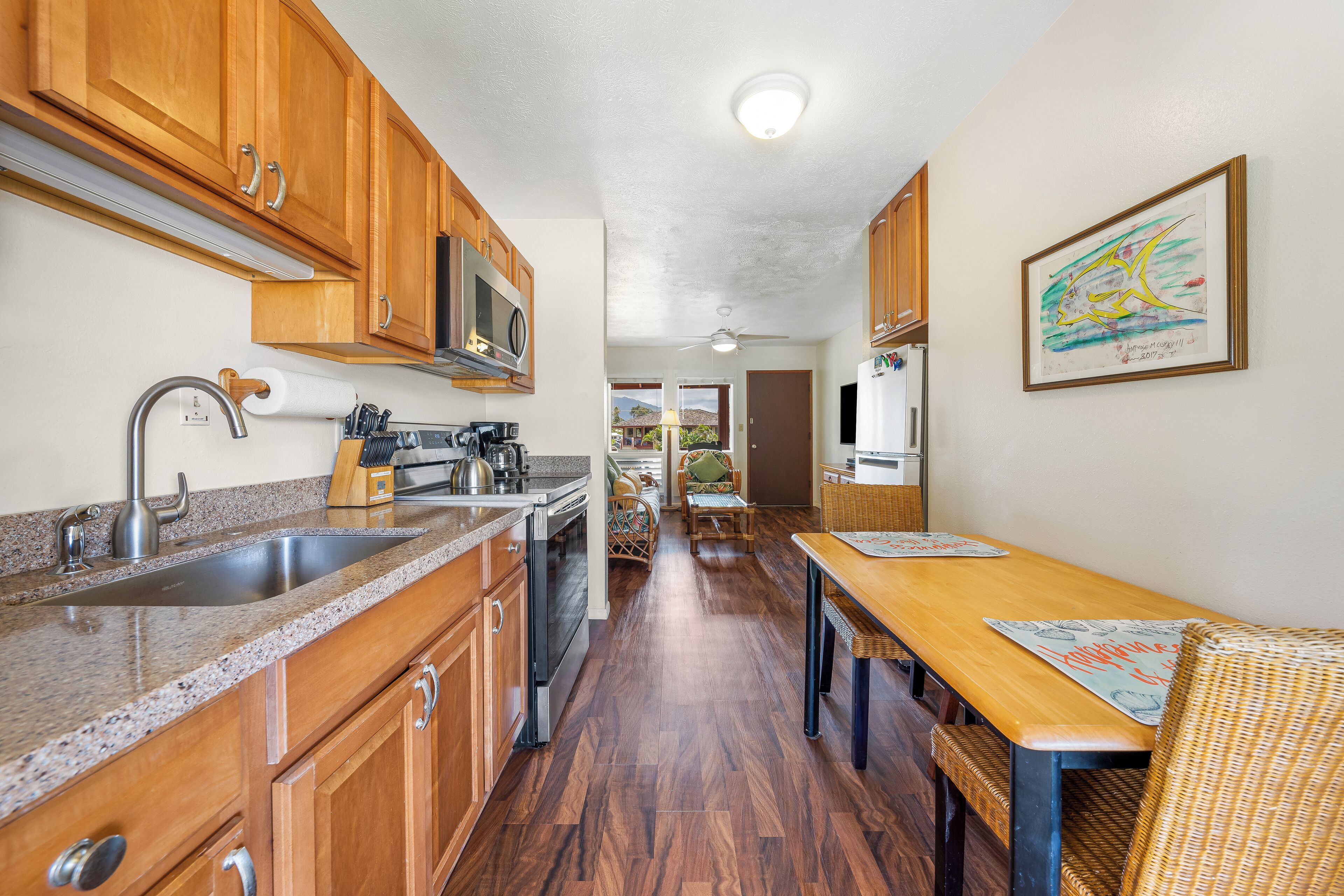 A kitchen with wooden cabinets, a stainless steel sink, and a microwave. There is a dining area with a wooden table and chairs.