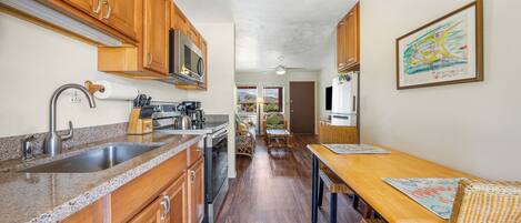 A kitchen with wooden cabinets, a stainless steel sink, and a microwave. There is a dining area with a wooden table and chairs.