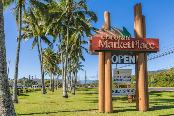 A sign for Coconut MarketPlace with a 'OPEN' sign, a 'NOW LEASING' sign, and a 'FREE HULA SHOW' sign.