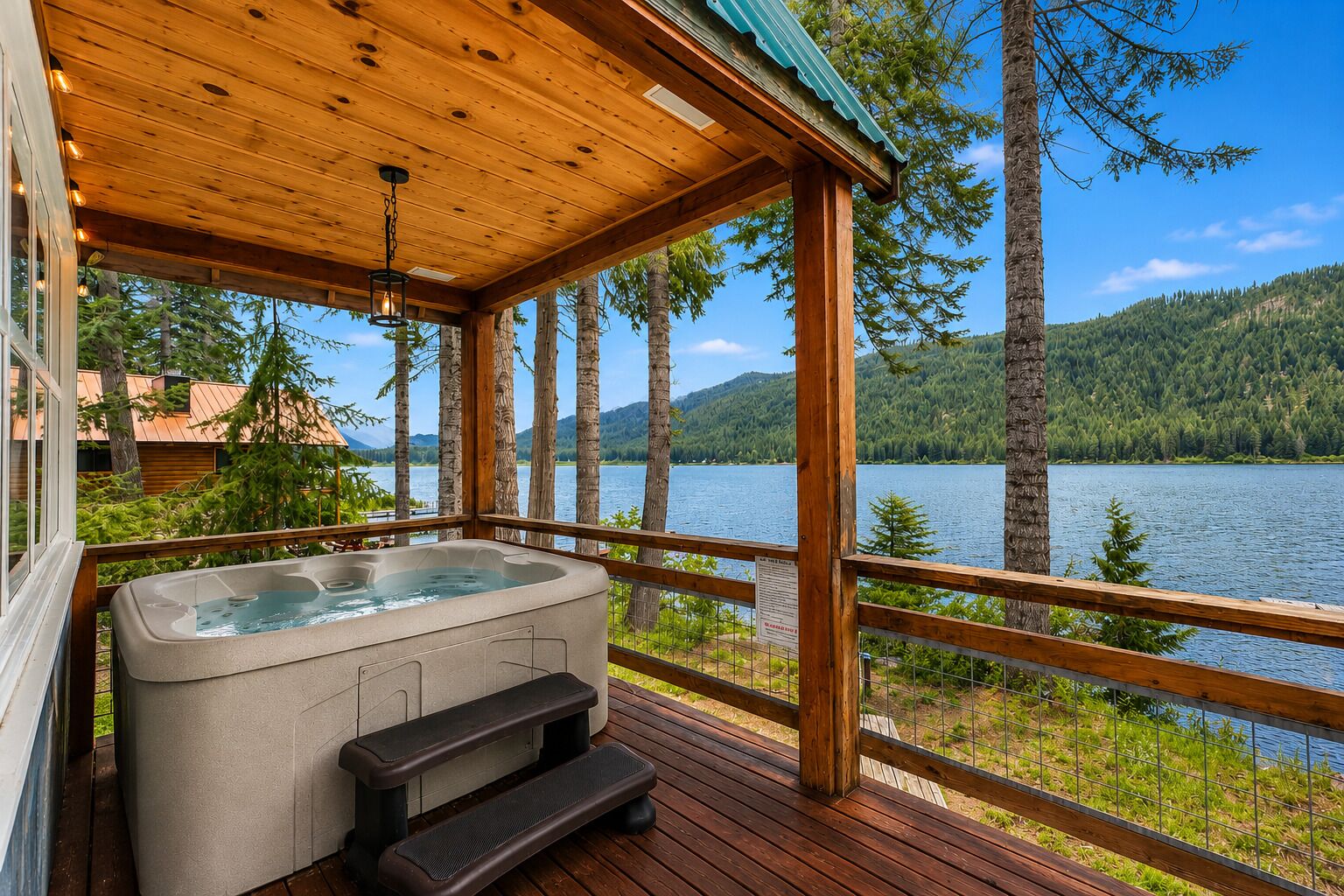 A wooden deck with a hot tub, wooden railing, and a view of a lake and forest.