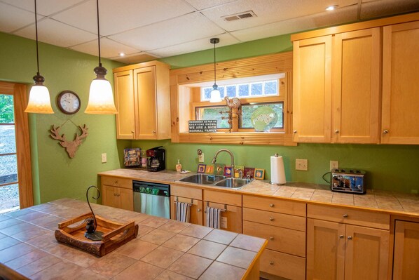 A kitchen with wooden cabinets, a sink, a window with a view, and a clock on the wall.