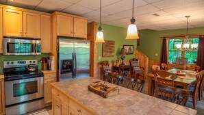 A kitchen with wooden cabinets, stainless steel appliances, a tiled island, and a dining area with wooden chairs and a table. - Rock n Rhapsody - Blue Ridge Log Cabin - Minutes to West Jefferson - Fireplace - Foosball (West Jefferson)