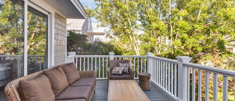 A covered outdoor deck with a wicker sofa, a wooden table, and wicker chairs.