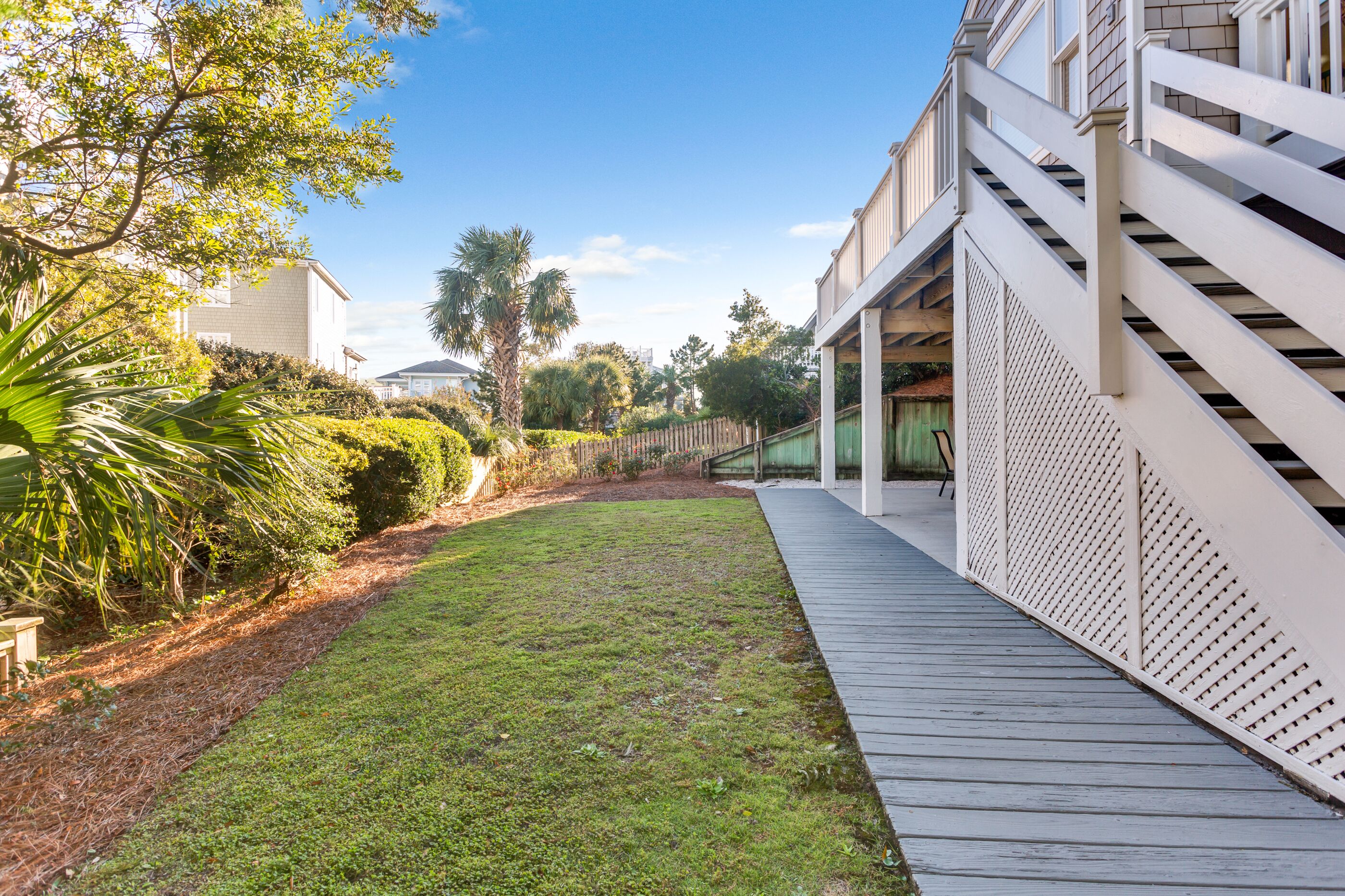 Una propiedad residencial con terraza de madera, césped y valla blanca.