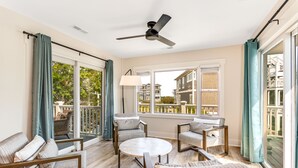 Una habitación iluminada por el sol, con ventilador de techo, ventanas grandes y vistas a un balcón.