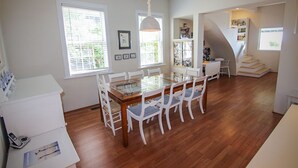 A dining area with a glass-top table, white chairs, and a staircase leading to a loft.