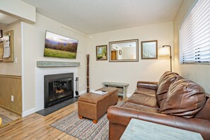 A living room with a fireplace, a television mounted above it, a brown leather sofa, and a small table with a lamp.