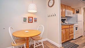 Una cocina con armarios de madera, un refrigerador blanco y un microondas. Hay una mesa de comedor con dos sillas y una lámpara colgante.