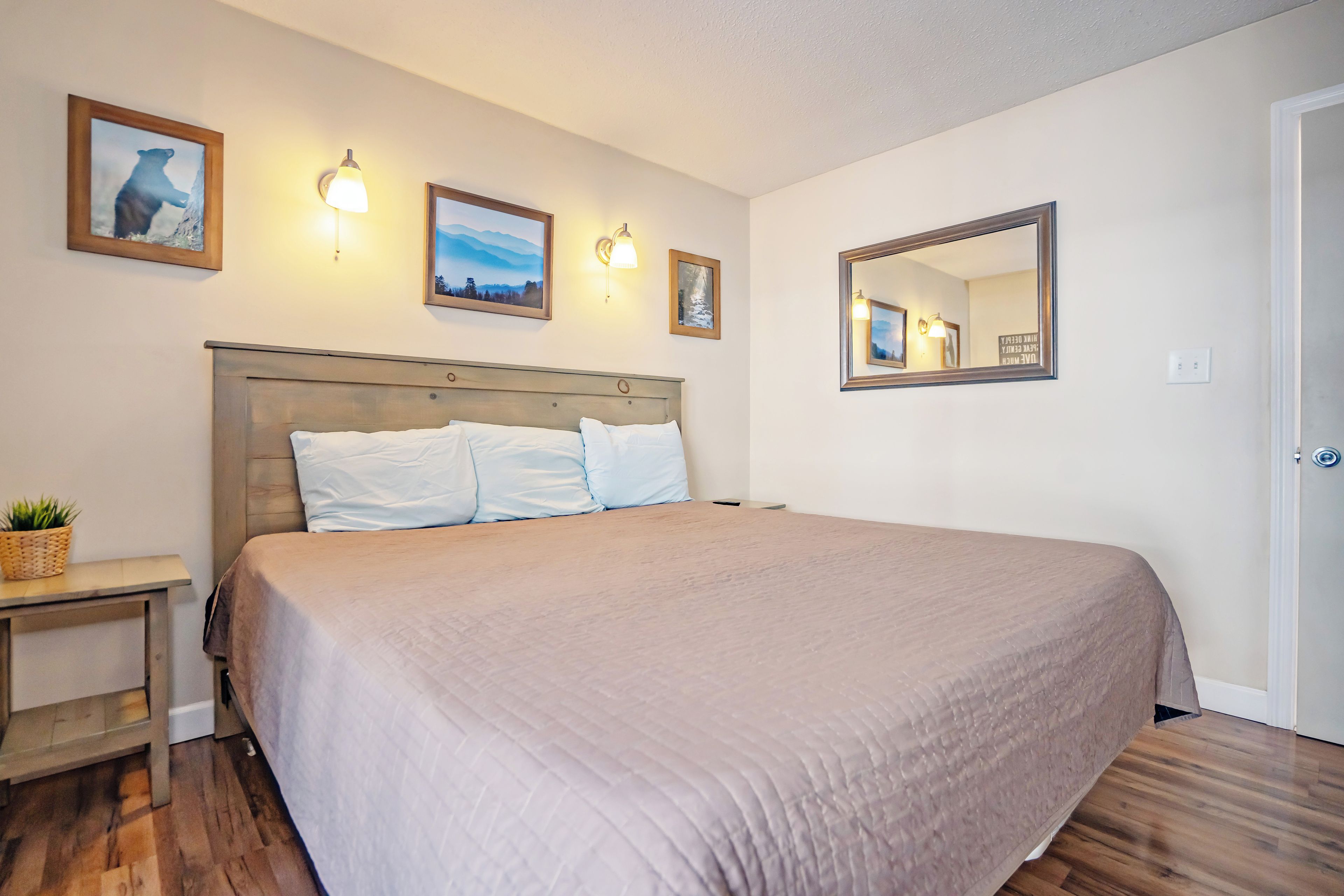 A hotel room with a large bed, a bedside table with a plant, and wall-mounted light fixtures.