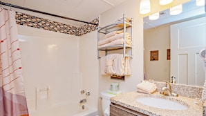 Un baño con bañera, inodoro y tocador con lavamanos y espejo.