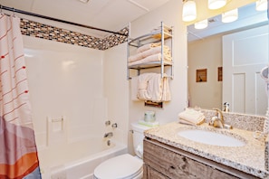 Un baño con bañera, inodoro y tocador con lavamanos y espejo.