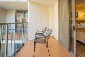 Ein Balkon mit Metallstühlen, eine Glastür, die in ein Schlafzimmer führt, und ein Blick auf Gebäude im Hintergrund.