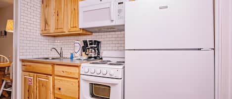 Cocina compacta con armarios de madera, un refrigerador blanco, una estufa y un microondas.