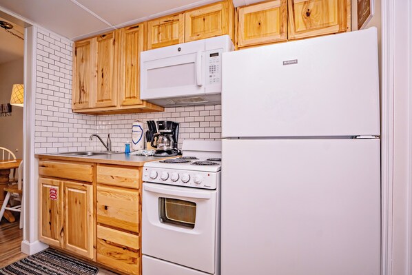 A compact kitchen with wooden cabinets, a white refrigerator, a stove, and a microwave.