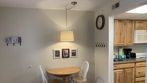A dining area with a wooden table and two chairs, a wall clock, and framed pictures.