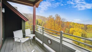 A balcony with two white chairs, a clock, and a view of autumn trees. - Gorgeous views, tastefully decorated Ski on/ski off 3 bedroom condo, Lodges 303 (Killington)
