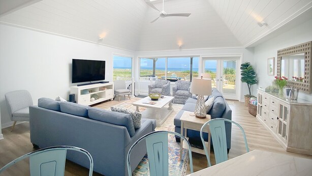 A spacious living room with a large TV, comfortable seating, a dining area, and a view of the ocean. - Wrightsville Beach Coastal Retreat (Wrightsville Beach)