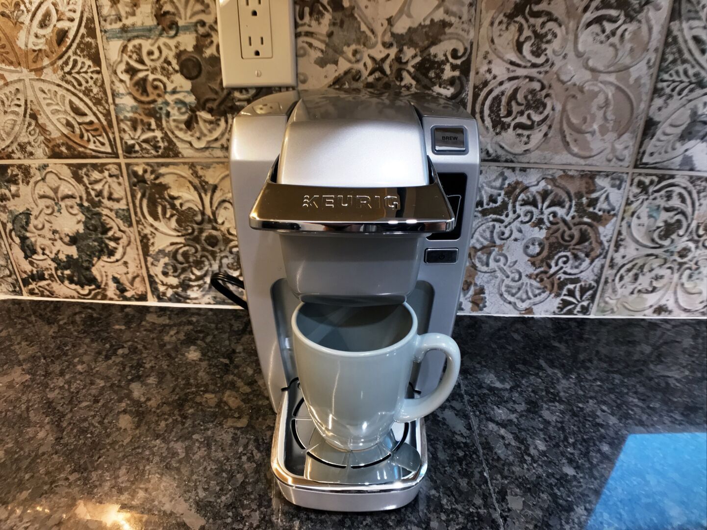 A Keurig coffee maker on a granite countertop with a patterned backsplash.