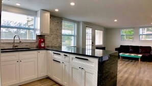 A modern kitchen with white cabinets, a black countertop, and a red coffee maker.