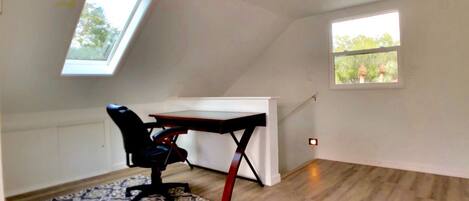 A small, sloped ceiling room with a desk and chair, a patterned rug, and two windows.