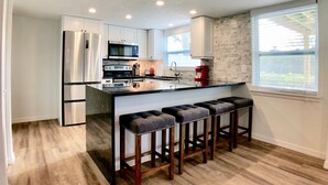 A modern kitchen with stainless steel appliances, a central island with bar stools, and a large window providing natural light.