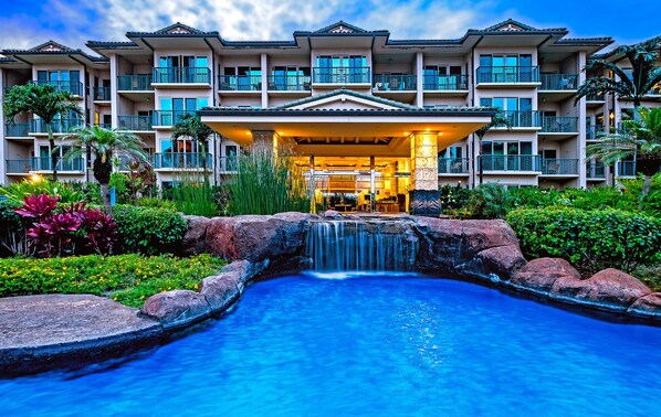 A hotel with a large pool, a waterfall, and lush greenery.
