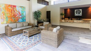 A lobby with wicker furniture, a colorful abstract painting, and a reception desk with a logo. - 1 Bedroom * HighSpeedConnection* Downtown quite & safe-5th ave steps away (Playa del Carmen)