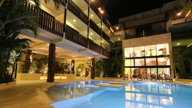 A swimming pool with a reflection, surrounded by a building with multiple balconies and indoor seating areas. - 1 Bedroom * HighSpeedConnection* Downtown quite & safe-5th ave steps away (Playa del Carmen)