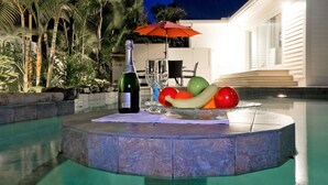 Escena a la piscina amb una ampolla de vi, gots i un bol de fruita.