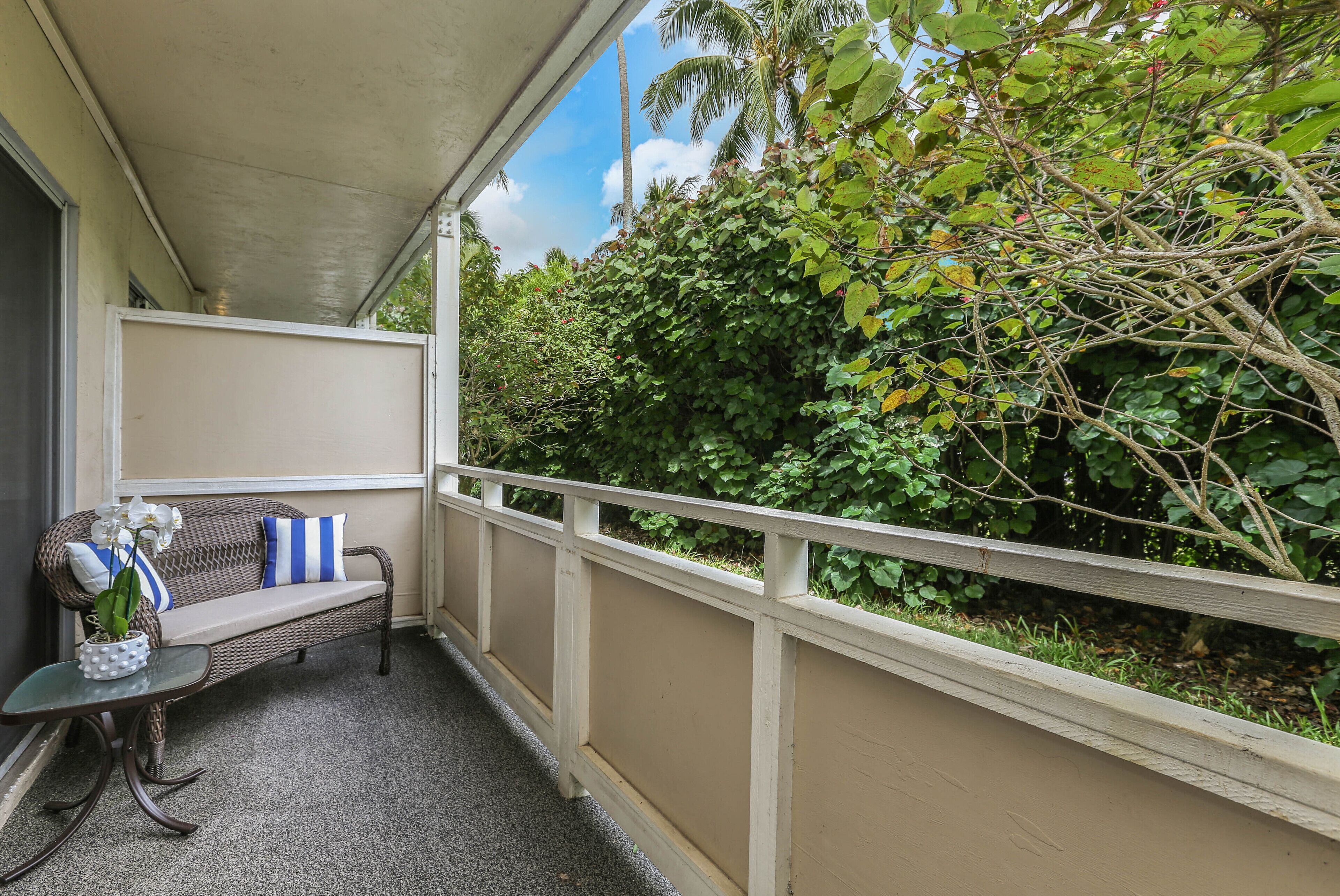 A covered balcony with a wicker sofa and a small table with a flower vase.