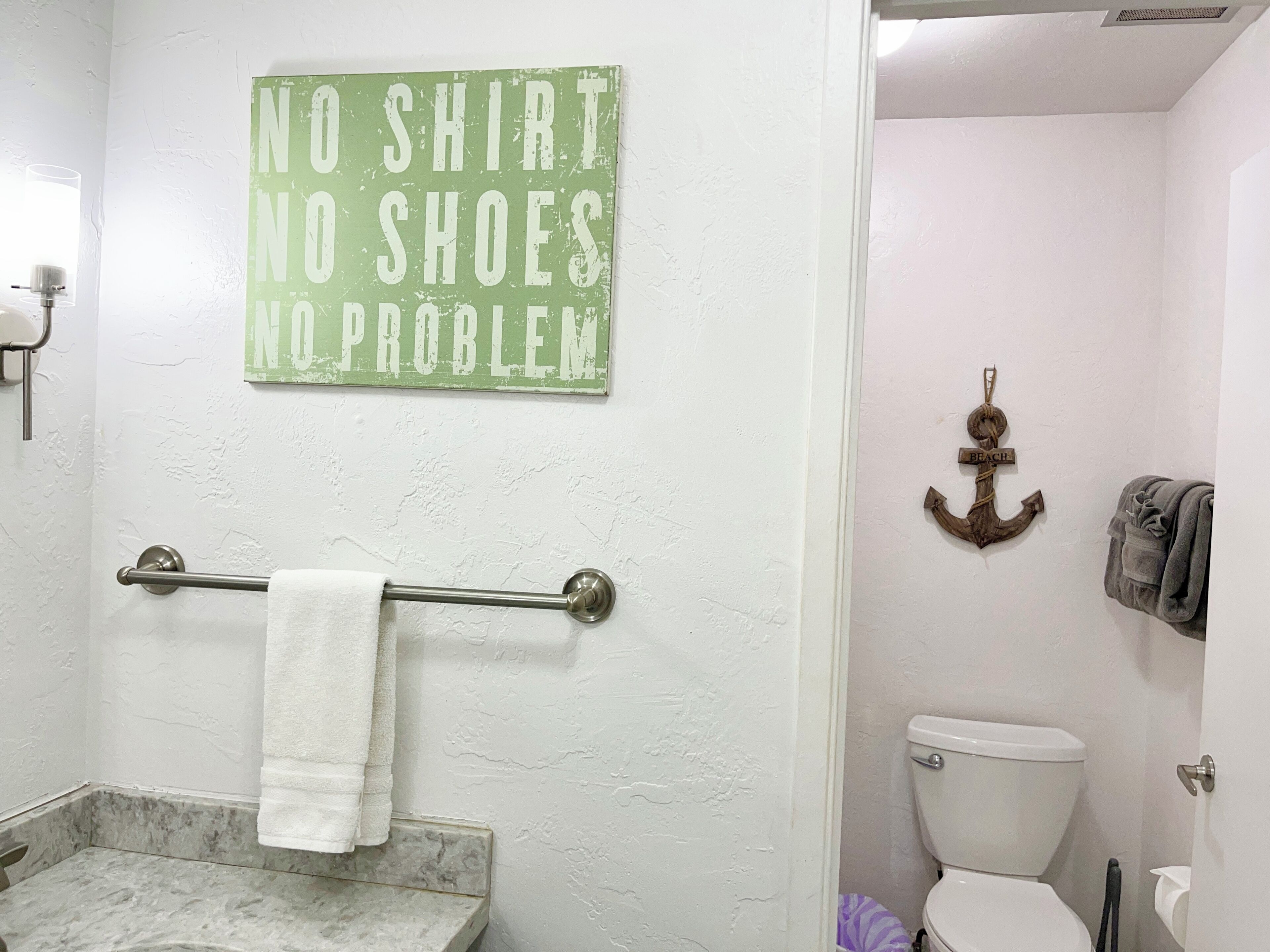 A bathroom with a towel rack, a toilet, and a sign that reads "NO SHIRT NO SHOES NO PROBLEM".