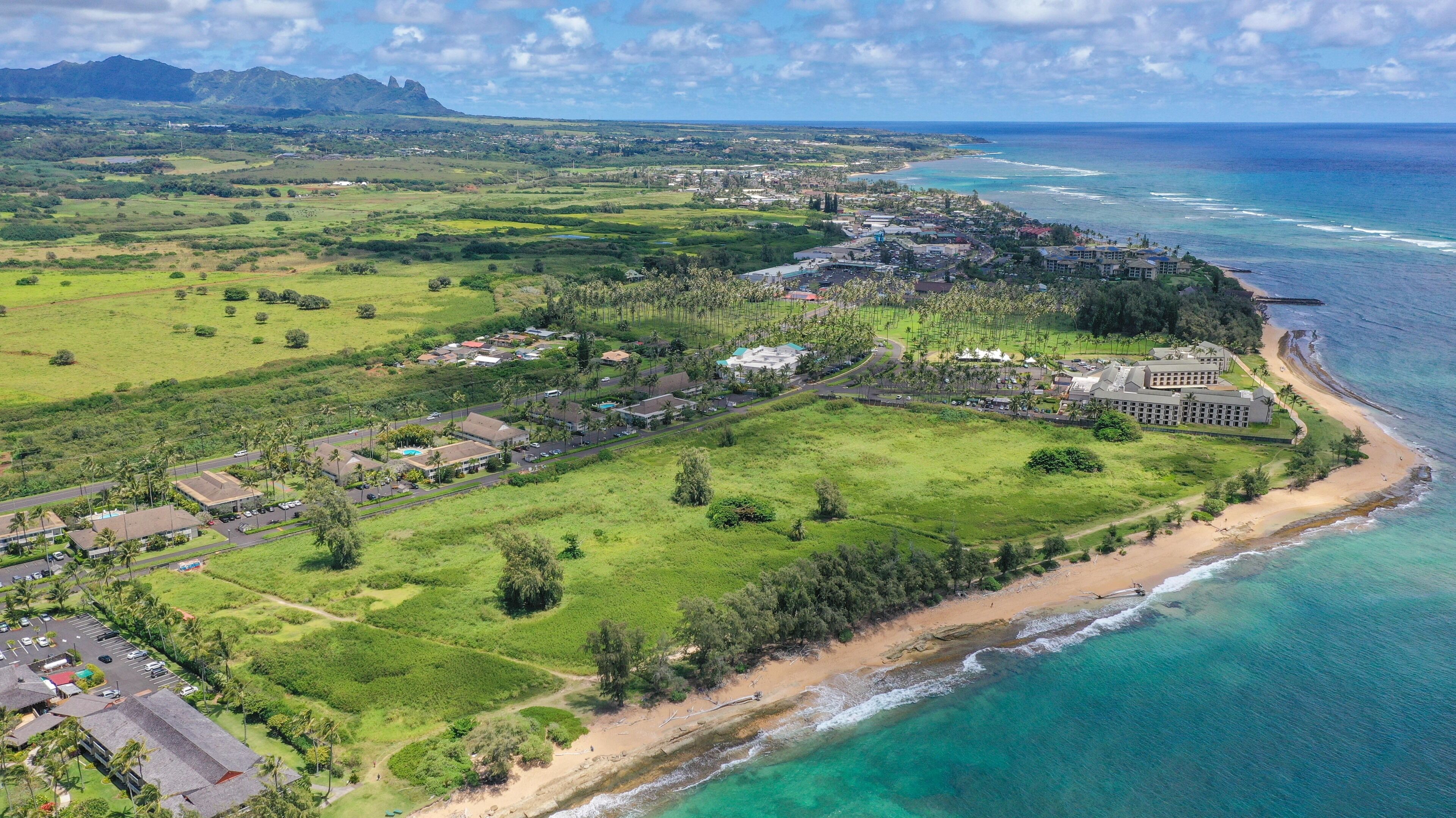 An aerial view of a coastal resort with a beachfront, a golf course, and a large hotel complex.