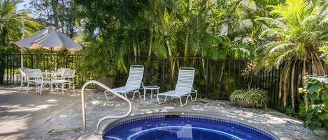 A swimming pool with a blue mosaic tile design, surrounded by white lounge chairs and a palm tree.