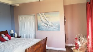 A bedroom with a bed, a nightstand, a wall-mounted artwork, a door, and a window with red curtains. - Large Custom Guest House On Hill Top Estate In Bonsall (Bonsall)