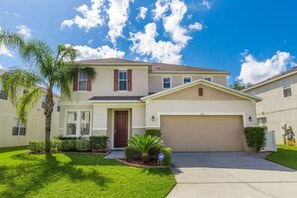A two-story house with a front garage, a well-maintained lawn, and a palm tree. - Palm Breeze: Private Pool/Spa & 24/7 Support! (Davenport)
