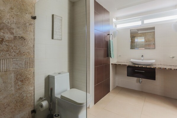 A bathroom with a glass shower enclosure, a toilet, a sink with a mirror above it, and a towel hanging on the wall.