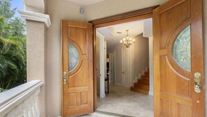 Eine beeindruckende Eingangshalle mit zwei Holztüren, die Glasscheiben aufweisen, einem marmoreingefassten Boden und einer Treppe, die in ein Obergeschoss führt.