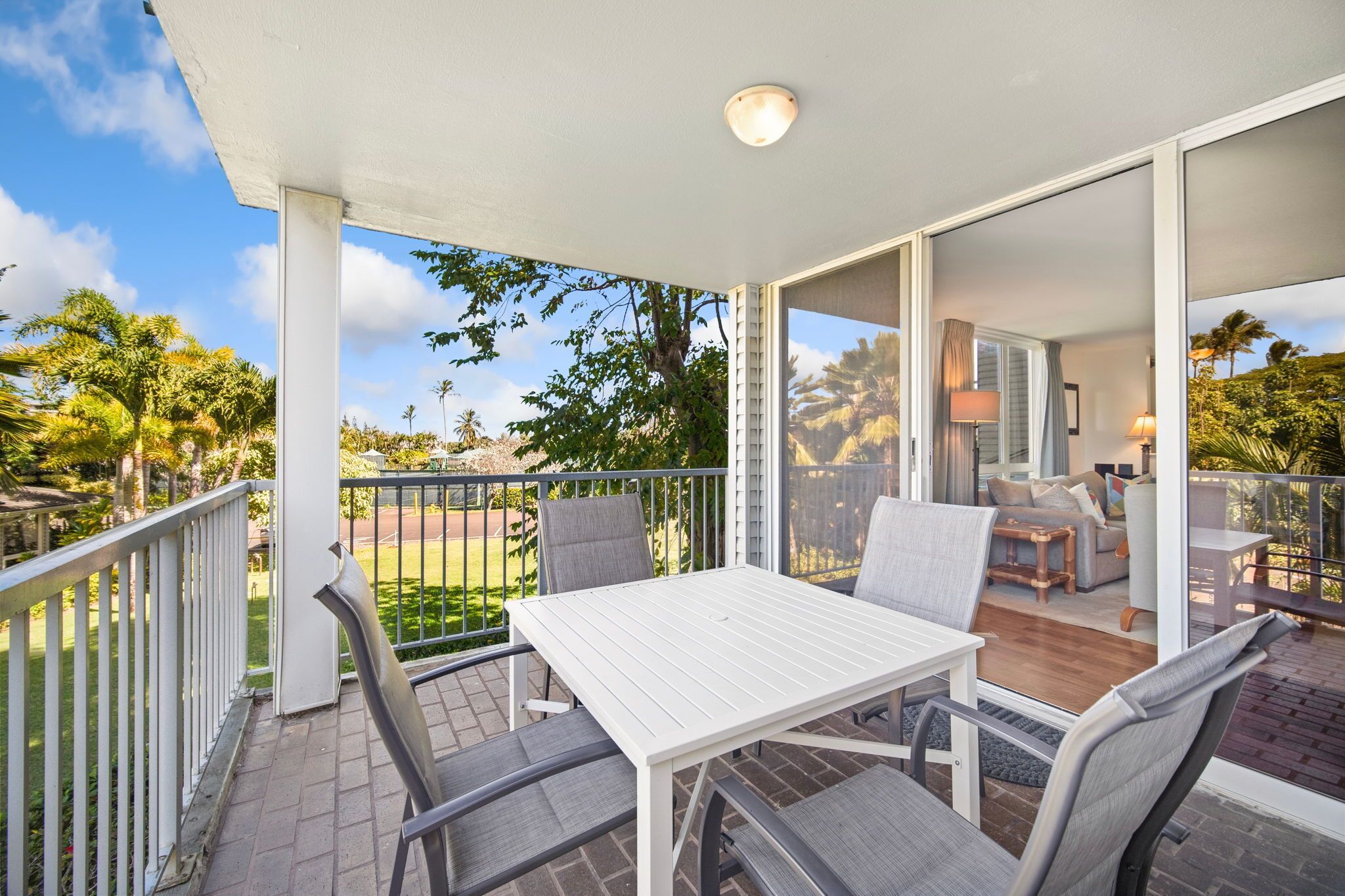 A covered outdoor seating area with a table and chairs, overlooking a garden and a building interior.