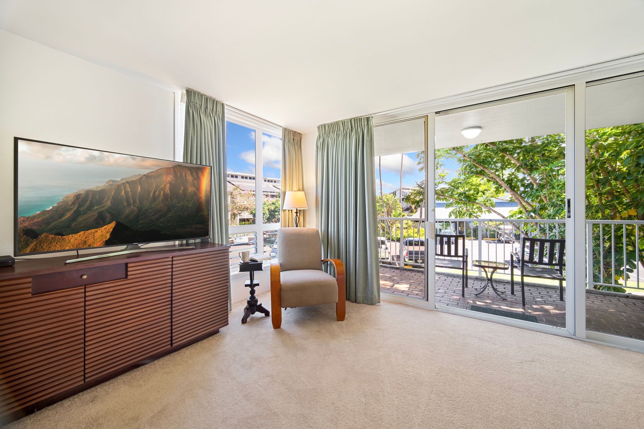 A living room with a TV, a chair, a small table, and a balcony with a view of the city.