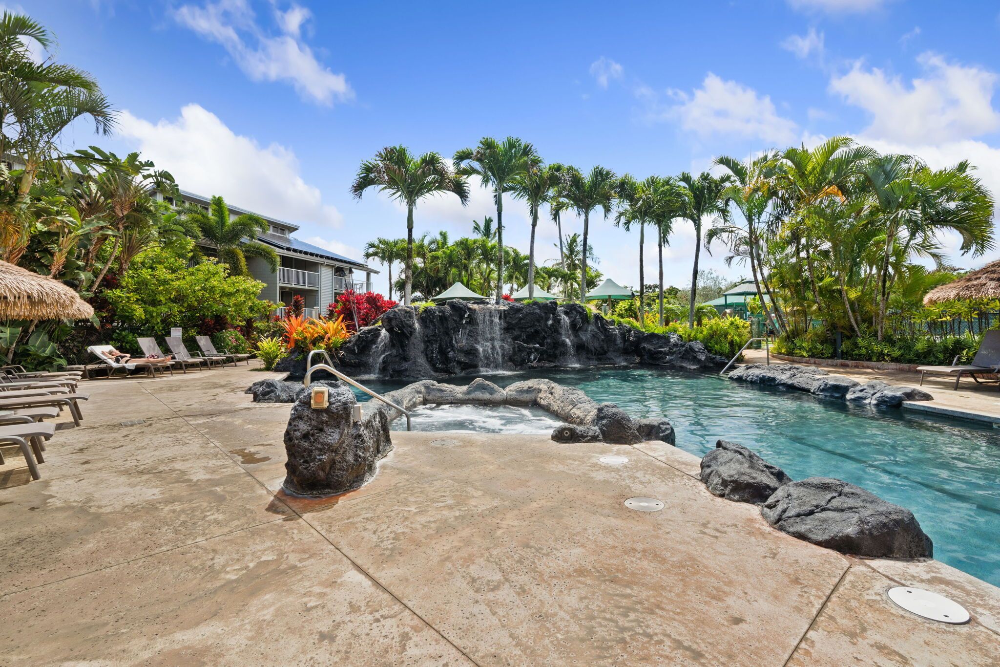 A pool area with lounge chairs, a waterfall, and tropical plants.