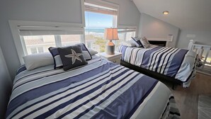 Une chambre avec deux lits, une literie à rayures, un coussin en forme d’étoile de mer, une lampe et une vue sur la plage.