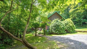 A rustic cabin surrounded by lush greenery, with a gravel path leading to it. - Creekside Escape | Hot Tub & Wooded Privacy | Prime West Jefferson Location (West Jefferson)