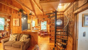 A cozy cabin interior with a wooden interior, a spiral staircase, and a dining area. - Creekside Escape | Hot Tub & Wooded Privacy | Prime West Jefferson Location (West Jefferson)