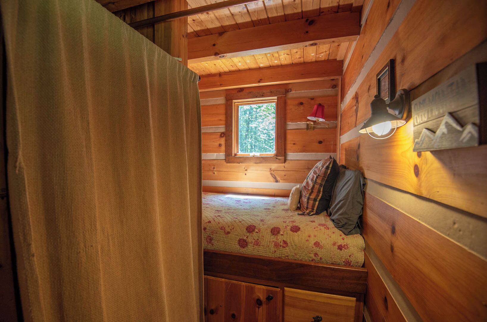 Ein gemütliches Blockhäuschenzimmer mit Bett, Fenster und Lampe.