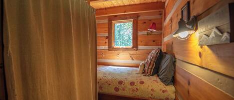 Ein gemütliches Blockhäuschenzimmer mit Bett, Fenster und Lampe.