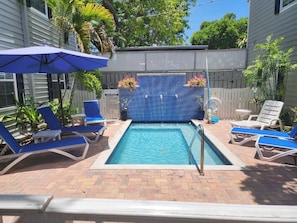 A swimming pool with blue tiles, surrounded by lounge chairs and an umbrella.