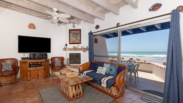 A living room with a TV, wooden furniture, a sofa with cushions, a ceiling fan, and a view of the ocean. - Buenos Tiempos – Beachfront, Sleeps 6, Rocky Point (Puerto Peñasco)