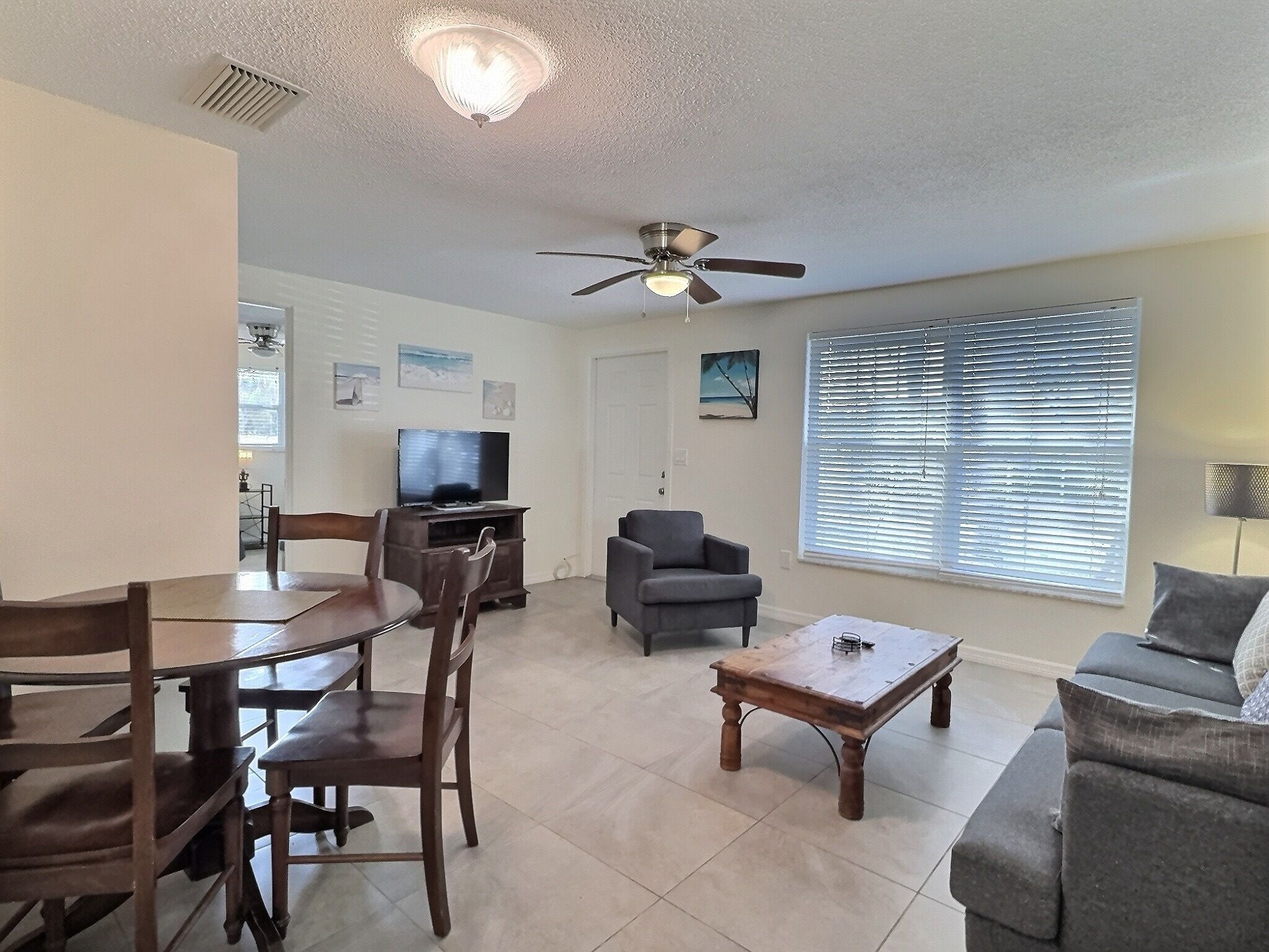 A living room with a dining table, chairs, a sofa, a TV, and a ceiling fan.